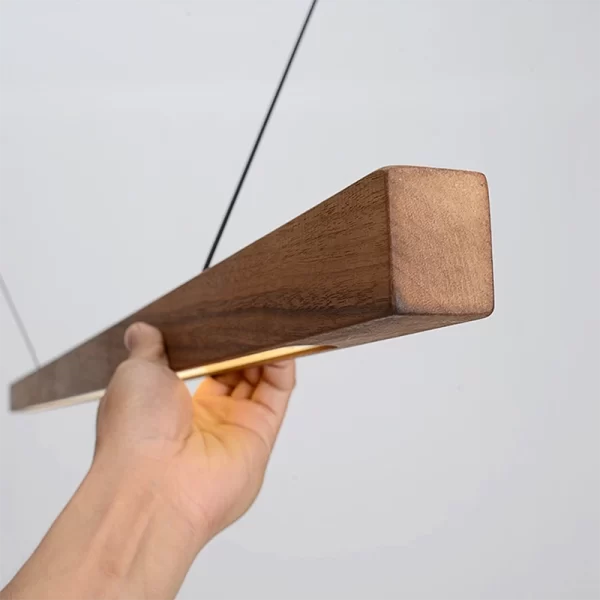 A hand holds a lit black walnut pendant light to display its side profile.