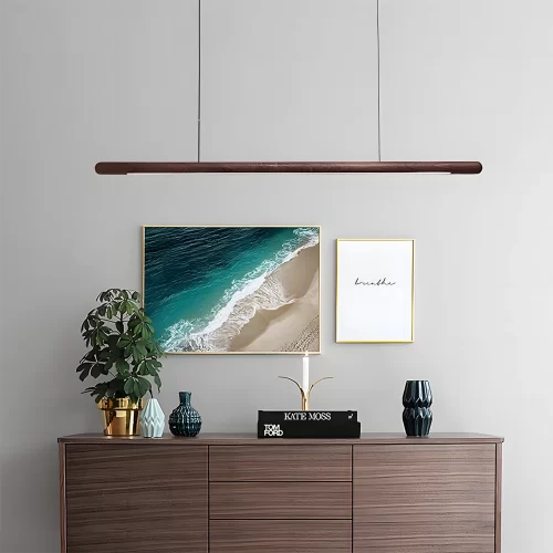 A circular walnut wood pendant light hangs from the corridor ceiling, with a brown table displaying plants and porcelain, adorned by two paintings on the walls.