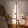 A hand holding a remote control adjusts the color temperature and brightness of a minimalist wooden LED floor light